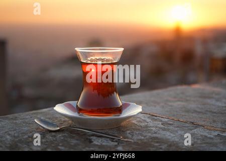 Verre traditionnel en forme de tulipe de thé noir turc au coucher du soleil, Mardin, Türkiye Banque D'Images