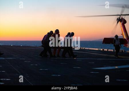 241120-N-IL330-1468 des marins et un membre de l'équipage d'un hélicoptère MH-60 Jayhawk de la Garde côtière évacuent médicalement un marin du pont d'envol à bord du porte-avions d'assaut amphibie USS Tripoli (LHA 7) pendant les opérations de vol, le 20 novembre 2024. Le Tripoli est un navire d'assaut amphibie de classe américaine, domicilié à San Diego. Tripoli est en cours dans la zone d'opérations de la 3e flotte des États-Unis menant une formation tactique avancée qui améliore la capacité de combat et la compétence tactique. (Photo de l'US Navy par Austyn Riley, spécialiste des communications de masse, 2e classe) Banque D'Images