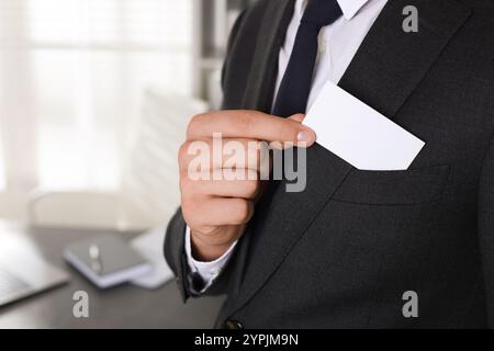 Homme prenant une carte de visite vierge de la poche de sa veste au bureau, gros plan. Maquette pour le design Banque D'Images