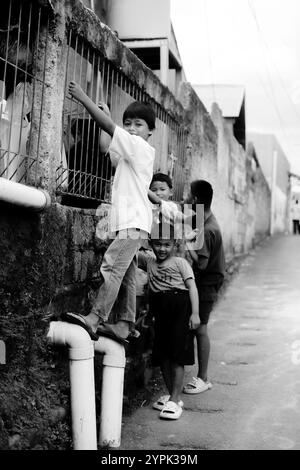 Bogor, 24 novembre 2024. Quatre jeunes enfants debout ensemble dans une ruelle étroite, souriant et regardant autour dans un cadre de quartier animé Banque D'Images