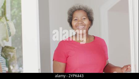 Souriante senior afro-américaine senior femme ouvrant la porte pour saluer le visiteur Banque D'Images