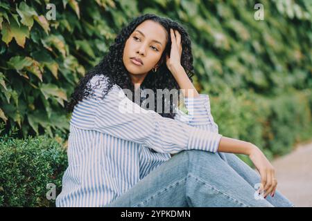 Une jeune femme contemplative se tient contre un mur de lierre vert luxuriant, entouré par la nature Banque D'Images