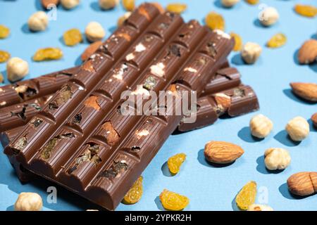 Barres de chocolat noisettes parmi les noix dispersées et les raisins secs sur un fond bleu. Banque D'Images