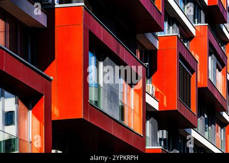 Façade d'appartement moderne avec panneaux rouge vif, fenêtres en verre et ombre et lumière ludiques Banque D'Images