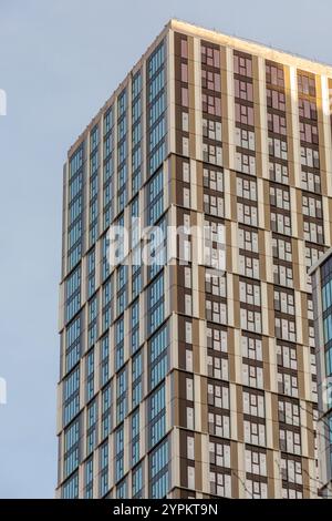 Façade moderne d'immeuble d'appartements à Canary Wharf avec motifs géométriques de fenêtres en verre et revêtement beige sur ciel dégagé Banque D'Images