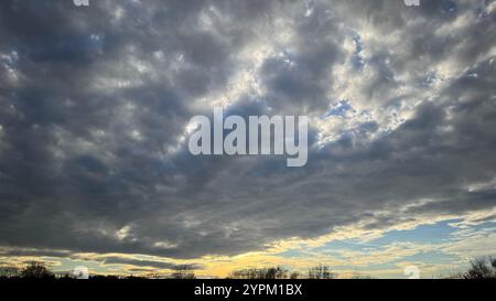 Ciel couvert avec principalement des nuages gris foncé et gris clair. Des taches de ciel bleu sont visibles à travers des ruptures dans la couverture nuageuse. Un horizon bas l Banque D'Images