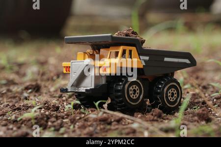 vue latérale du modèle de jouet jaune de petit camion à benne basculante transportant du sol sur le sol. image conceptuelle de l'industrie minière ou de la construction. Banque D'Images