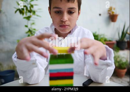 Un jeune garçon intensément concentré sur la construction d'une tour avec des blocs colorés. La scène se déroule dans un jardin paisible, soulignant sa concentration et sa créa Banque D'Images