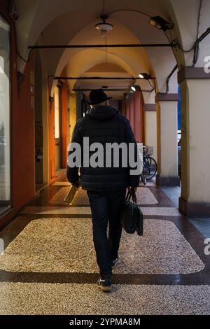 Bologne, Italie. 8 octobre 2024 - Un homme marche dans une arcade tranquille, portant un sac et une bouteille Banque D'Images