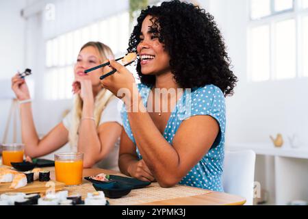 Groupe multiethnique de jeunes amis se réunissant à la maison et mangeant des sushis - personnes heureuses multiraciales se liant tout en déjeunant Banque D'Images