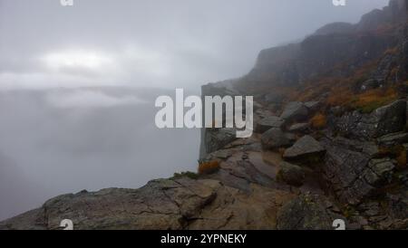 Une personne marche le long d'une falaise rocheuse enveloppée de brouillard, créant une atmosphère mystérieuse et aventureuse. Banque D'Images