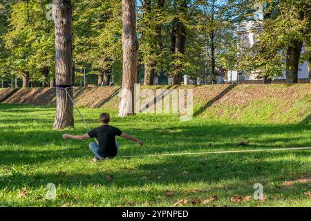 Un homme est assis sur une corde tendue entre deux arbres dans un parc de la ville, Pise, Italie Banque D'Images