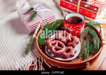 Plateau avec café et pain d'épices au chocolat sous sapin de Noël décoré par des cadeaux emballés. Gros plan sur une boisson de fête confortable. Tasse habillée Banque D'Images