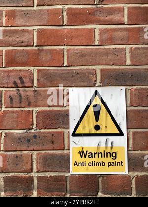 Un panneau d'avertissement sur un mur de briques rouges conseillant l'utilisation de peinture anti-escalade, sur le panneau et sur le mur sont des traînées de doigts noires Banque D'Images