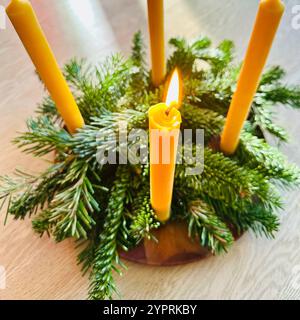 Une couronne de l'Avent faite avec des brins de sapin et avec quatre bougies jaunes en cire d'abeille, l'une d'elles est allumée Banque D'Images