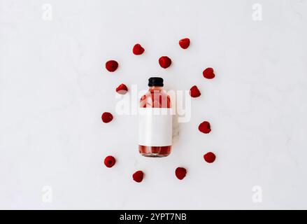 Bouteille en verre avec des bouchons noirs, kombucha rouge fourré et framboises ingrédients sur fond blanc. Petite bouteille avec étiquette blanche. Vue de dessus. Banque D'Images
