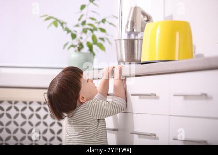 Petit garçon jouant avec le grille-pain dans la cuisine. Situation dangereuse Banque D'Images