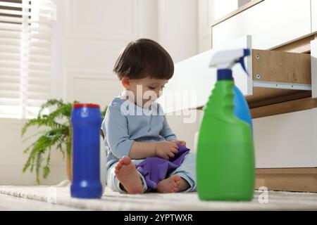 Petit garçon jouant avec un gant parmi les bouteilles de détergents près de l'armoire à la maison. Enfant en danger Banque D'Images