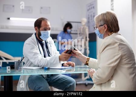 La vieille femme caucasienne écoute attentivement que le médecin portant le stéthoscope offre la bouteille de pilule de prescription et explique les effets de médicament pendant la consultation. Le patient retraité reçoit des médicaments du médecin. Banque D'Images