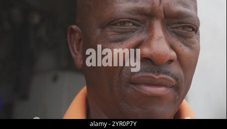 Portrait gros plan d'un homme africain dans un township, portant une chemise orange et penchant en avant slow Mo Banque D'Images