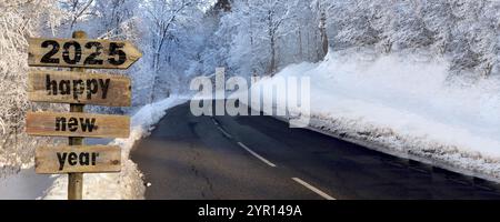 2025 BONNE ANNÉE écrit sur panneau en bois avec flèche pointant vers une route traversant une forêt enneigée dans la montagne alpine Banque D'Images