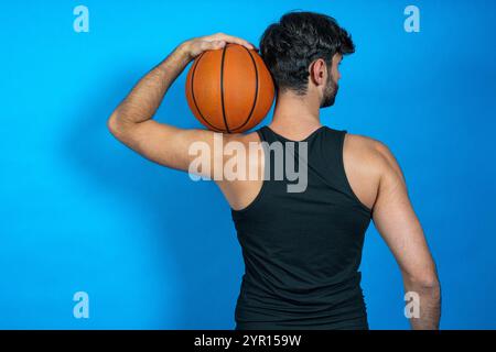 Athlète masculin tenant un ballon de basket-ball sur son épaule, mettant en valeur sa force et son athlétisme Banque D'Images