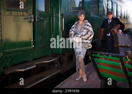 Scène de reconstitution sur la plate-forme près d'un authentique wagon de première classe 1927 où une femme posh 1920s attend ses bagages Banque D'Images