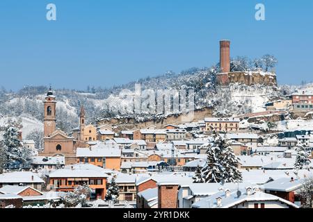 Un pittoresque village italien enneigé de Corneliano d'Alba en hiver, avec une architecture historique et une tour médiévale sous un ciel bleu clair. Banque D'Images