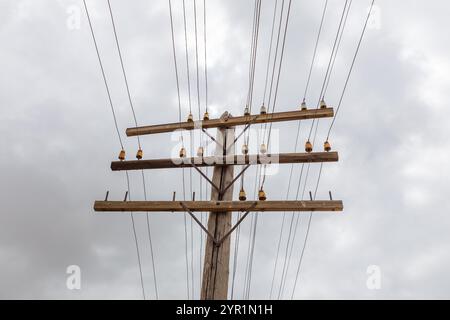 La ligne aérienne de communication s'étend entre les poteaux électriques sous un ciel gris, avec de multiples isolants visibles reliant les fils. Banque D'Images