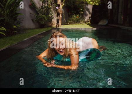 Femme heureuse se relaxant sur l'anneau gonflable à la piscine pendant la journée ensoleillée Banque D'Images