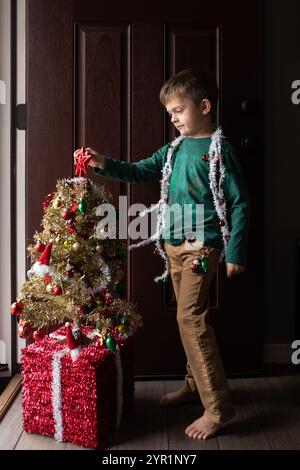 Jeune garçon décorant un petit arbre de Noël près de la porte Banque D'Images