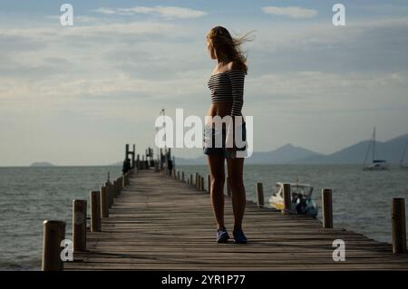 Femme debout sur la jetée au-dessus de la mer contre le ciel pendant le coucher du soleil Banque D'Images