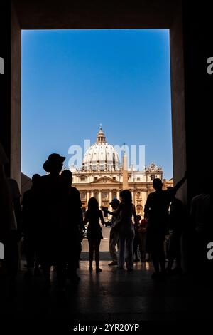 Les touristes passent par une arche, révélant la basilique Saint-Pierre sous un ciel dégagé de la Cité du Vatican, mettant en valeur sa grande architecture. Banque D'Images