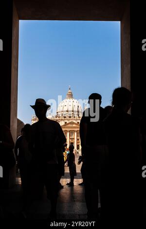 Les touristes passent par une arche, révélant la basilique Saint-Pierre sous un ciel dégagé de la Cité du Vatican, mettant en valeur sa grande architecture. Banque D'Images