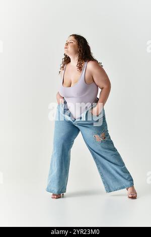 Jeune femme pose en toute confiance dans un Jean oversize et un haut ajusté sur un fond minimaliste. Banque D'Images