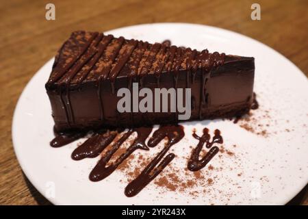 Une tranche décadente de gâteau au chocolat garnie d'un riche filet de chocolat, servi sur une assiette blanche, parfait pour les amateurs de desserts et de gourmandises sucrées. Banque D'Images