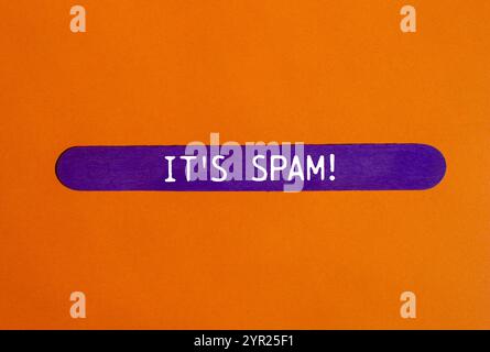 C'est un message de spam écrit sur un bâton de bois violet avec un fond orange. Conceptuel, c'est le symbole spam. Copier l'espace. Banque D'Images