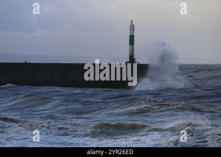 Aberystwyth Wales UK Météo 2 décembre 2024. Un matin d'hiver froid et bruyant autour de la côte galloise, de grandes vagues s'écrasent sur les défenses maritimes et la lumière du port avec un ciel rose au-dessus de la tête, crédit : mike davies/Alamy Live News Banque D'Images