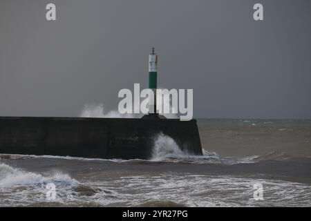 Aberystwyth Wales UK Météo 2 décembre 2024. Un matin d'hiver froid et bruyant autour de la côte galloise, de grandes vagues s'écrasent sur les défenses maritimes et la lumière du port avec un ciel rose au-dessus de la tête, crédit : mike davies/Alamy Live News Banque D'Images