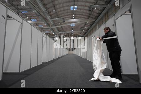 02 décembre 2024, Hambourg : un homme pose un rideau pour l'entrée d'une cabane lors de l'événement médiatique dans le logement des réfugiés dans le Hall B5 sur le terrain d'exposition. À partir du 3 décembre, le Hall B5 deviendra à nouveau un hébergement d’urgence pour les réfugiés. L'occupation est prévue pour jusqu'à 300 personnes, avec une capacité d'urgence totale de 476 places dans les compartiments. Le logement sera géré par l’entreprise sociale municipale Fördern & Wohnen. Photo : Marcus Brandt/dpa Banque D'Images