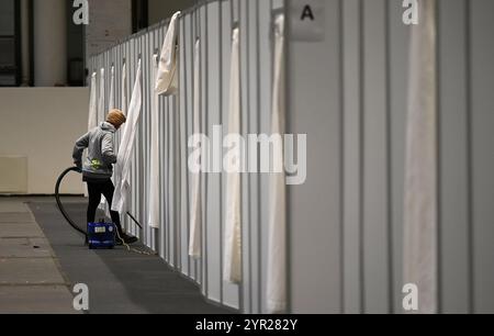 02 décembre 2024, Hambourg : une femme passe l'aspirateur dans une cabine temporaire lors de l'événement médiatique dans le logement des réfugiés dans le Hall B5 sur le terrain d'exposition. À partir du 3 décembre, le Hall B5 deviendra à nouveau un hébergement d’urgence pour les réfugiés. L'occupation est prévue pour jusqu'à 300 personnes, avec une capacité d'urgence totale de 476 places dans les compartiments. Le logement sera géré par l’entreprise sociale municipale Fördern & Wohnen. Photo : Niklas Graeber/dpa Banque D'Images