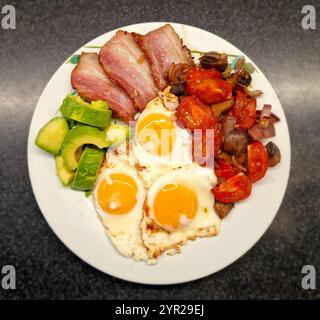 Assiette déjeuner décorée avec des ingrédients à faible teneur en glucides tels que du bacon frit avec des œufs frits, à côté d'une salade de champignons frits, tomates et oignons Banque D'Images