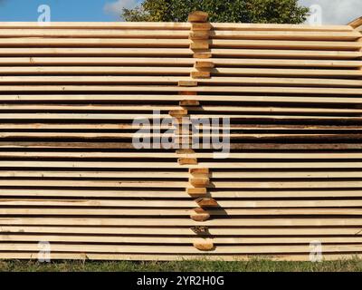 empiler des planches rabotées dans une usine ou un chantier de construction à l'extérieur, des planches empilées les unes sur les autres avec des barres transversales, créant une texture naturelle Banque D'Images