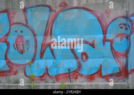 A lettres bleues et grises et épaisses lignes rouges et cerises avec bordures rouges. Un graffiti représentant le mot KOWAH est sur une clôture en béton grise et brune. Banque D'Images