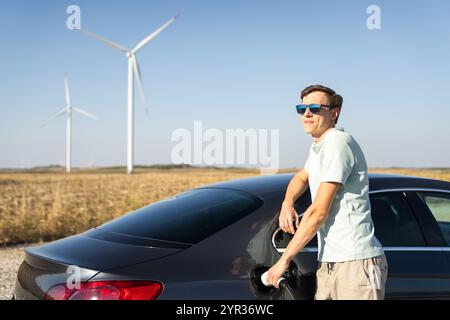 Homme avec voiture électrique de charge. Éoliennes en arrière-plan. Banque D'Images