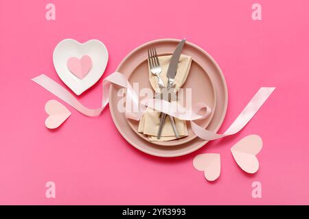 Table de réglage pour la Saint-Valentin avec serviette, ruban et coeurs en papier sur fond rose Banque D'Images