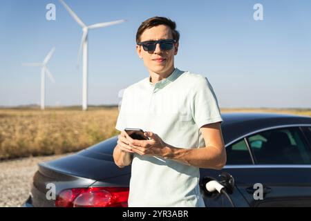 Homme avec voiture électrique de charge. Éoliennes en arrière-plan. Banque D'Images