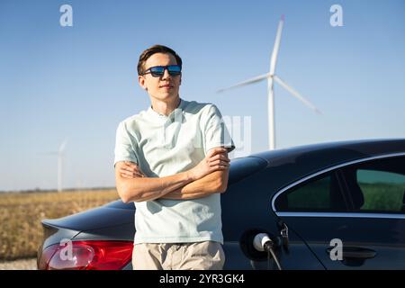 Homme avec voiture électrique de charge. Éoliennes en arrière-plan. Banque D'Images