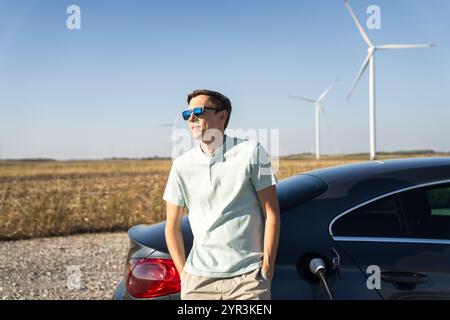 Homme avec voiture électrique de charge. Éoliennes en arrière-plan. Banque D'Images