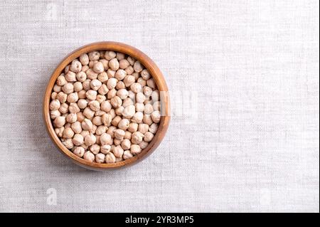 Pois chiches séchés dans un bol en bois, sur tissu de lin, avec un espace vide pour le texte. Pois chiches entiers et légèrement bronzés, légumineuse riche en protéines. Banque D'Images